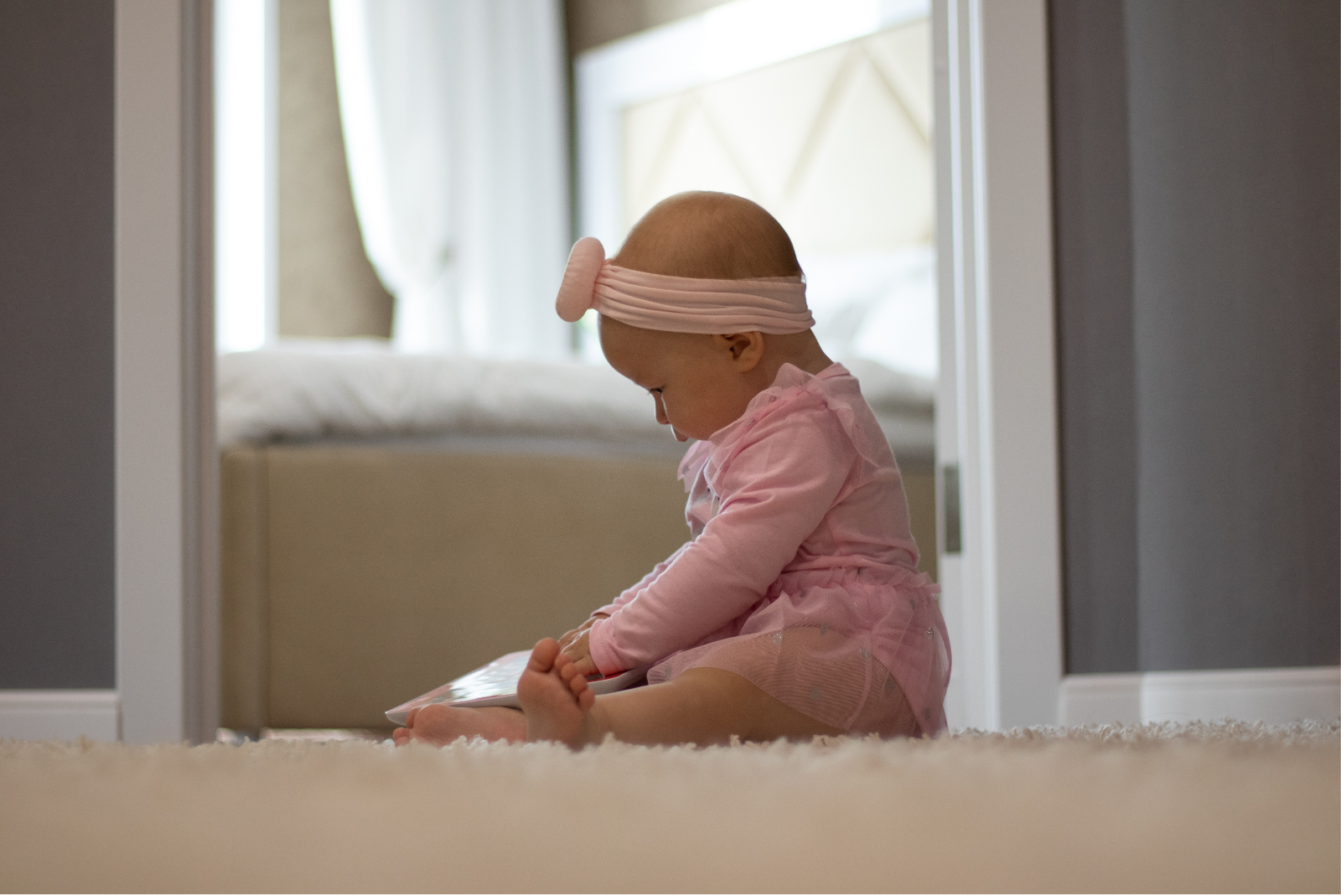 Bébé en grenouillère rose assis sur un drap blanc